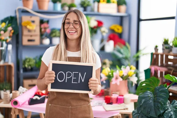 Young blonde woman working at florist holding open sign winking looking at the camera with sexy expression, cheerful and happy face.