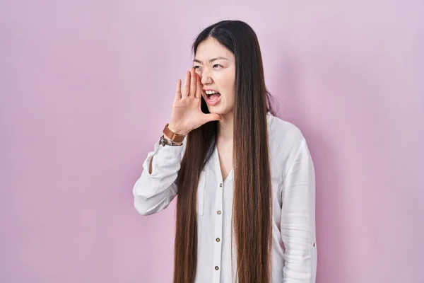 中国の若い女性ピンクの背景に叫んで立っていると口の上に手で横に大声で叫ぶ コミュニケーションの概念 — ストック写真