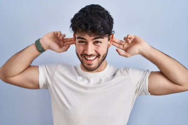 一个留着胡子的西班牙男人站在白色的背景上微笑着 用手指拉耳朵 做着滑稽的手势 试镜问题 — 图库照片