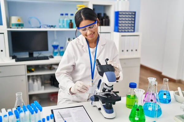 实验室显微镜下身穿科学家制服的年轻拉丁女子 — 图库照片