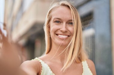 Genç sarışın kadın gülümsüyor. Kendine güveni tam. Kameranın önünde özçekim yapıyor.