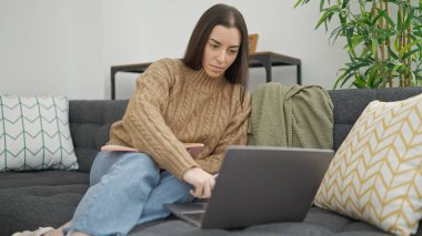 Evdeki kanepede dizüstü bilgisayar kullanan güzel İspanyol kadın.