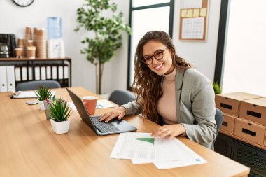 Young beautiful hispanic woman business worker using laptop reading document at office