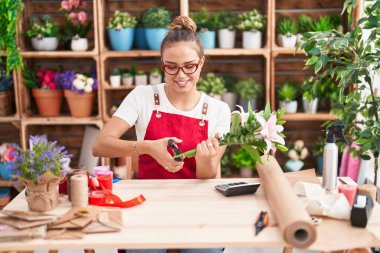Young beautiful hispanic woman florist cutting stem at florist