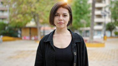 Young caucasian woman standing with serious expression at park