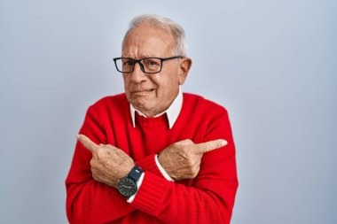 Senior man with grey hair standing over isolated background pointing to both sides with fingers, different direction disagree 