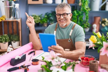 Çiçekçide çalışan, gri saçlı İspanyol bir adam. Tabletle video çekiyor. Gülümsüyor. 