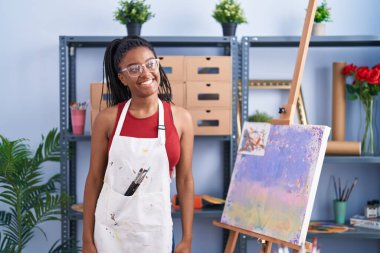 Sanat stüdyosunda örgü ören genç Afro-Amerikalı tuvali boyayıp yüzünde gülümsemeyle, doğal ifadeyle yan yana bakıyor. Kendinden emin gülen. 