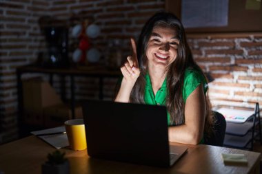 Gece ofiste çalışan genç bir kız bir numaralı parmağını gösterip işaret ederken kendinden emin ve mutlu bir şekilde gülümsüyor.. 