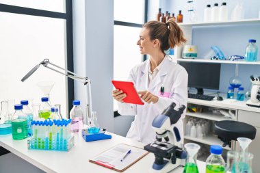 Laboratuvarda dokunmatik ped kullanan bilim adamı üniforması giyen genç bir kadın.