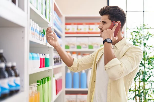 他的年轻顾客在药店用智能手机拿着药瓶说话 — 图库照片