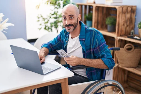 Young Hispanic Man Using Laptop Holdig Dollars Sitting Wheelchair Home — Stock Photo, Image