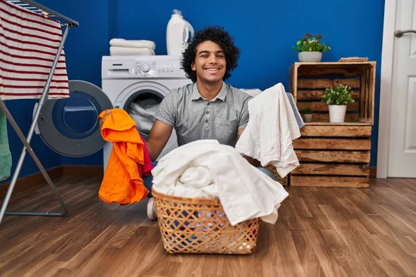 身穿卷发的西班牙裔男子在洗衣房洗衣服时眨眼看着摄像机 脸上带着性感的表情 快乐的表情 — 图库照片