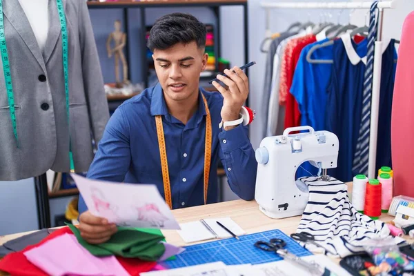 若いヒスパニック男は服工場でスマートフォンを見て服のデザインについて話して調整 — ストック写真