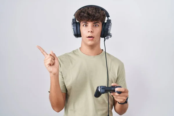 Adolescente Hispânico Jogando Vídeo Game Segurando Controlador Surpreso Apontando Com — Fotografia de Stock
