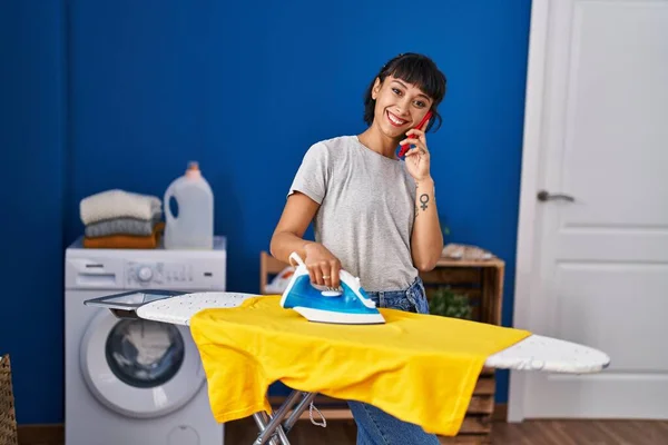 Çamaşırhanede Çamaşırları Ütüleyen Akıllı Telefonda Konuşan Genç Bir Kadın — Stok fotoğraf