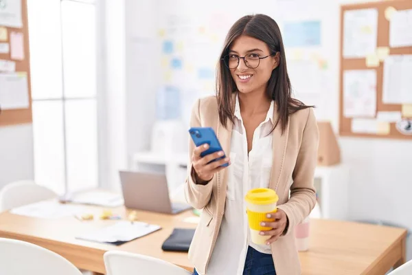 オフィスでスマートフォンのコーヒーを使用して若い美しいヒスパニック系女性のビジネスワーカー — ストック写真