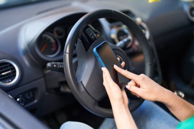 Genç İspanyol kadın akıllı telefon kullanıyor. Sokakta arabada oturuyor.