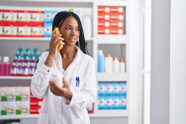 Afrika kökenli Amerikalı kadın eczacı eczanede elinde haplarla akıllı telefondan konuşuyor.