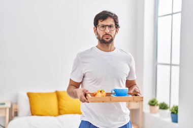 Handsome latin man eating breakfast on the bed skeptic and nervous, frowning upset because of problem. negative person. 