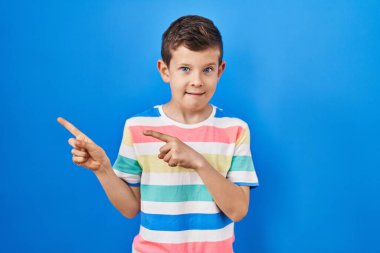 Mavi arka planda dikilen genç beyaz çocuk iki eliyle endişeli ve gergin, endişeli ve şaşırmış ifadesini işaret ediyor. 