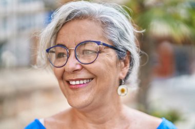 Middle age grey-haired woman smiling confident looking to the side at street