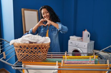 Genç Asyalı kadın çamaşır ipine giysilerini asıyor. Aşkla gülümsüyor. Elleriyle kalp sembolü yapıyor. romantik kavram. 