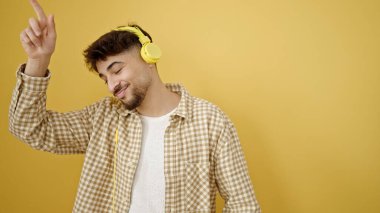 Genç Arap adam izole edilmiş sarı arka planda dans eden müzik dinliyor.