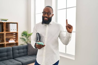 Terapi ofisinde çalışan Afro-Amerikalı bir adam akıllı telefon kullanarak gülümsüyor ve bir numaralı soru işareti olarak mutlu bir yüzü gösteriyor. 