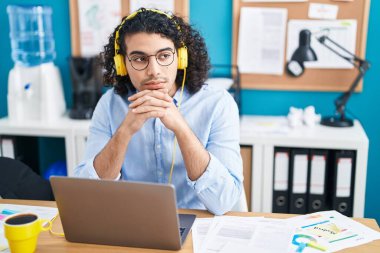 Ofiste çalışan dizüstü bilgisayar ve kulaklık kullanan genç Latin bir iş adamı.