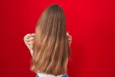 Kafkasyalı genç bir kadın kırmızı arka planda dikilip kendine sarılıyor mutlu ve pozitifken. Sevgi ve özgüven. 