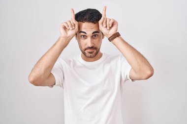 Beyaz arka planda duran yakışıklı İspanyol, boynuzları gibi parmağıyla komik hareketler yapıyor. 
