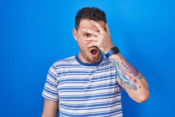 Young Hispanic Man Standing Blue Background Peeking Shock Covering Face — Stockfoto