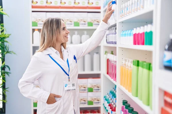 Young Blonde Woman Pharmacist Smiling Confident Holding Product Shelving Pharmacy — 图库照片