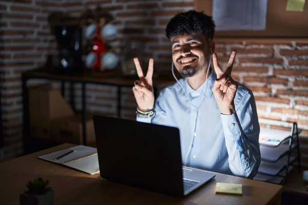 Geceleri Ofiste Çalışan Sakallı Gülümseyen Parmaklarını Zafer Işareti Yaparken Gösteren — Stok fotoğraf