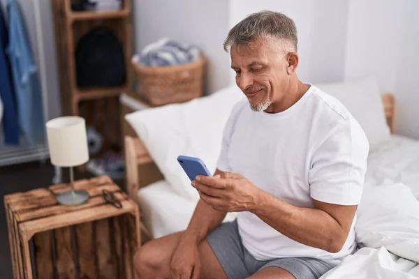 Medelålders Gråhårig Man Med Smartphone Sittande Sängen Sovrummet — Stockfoto