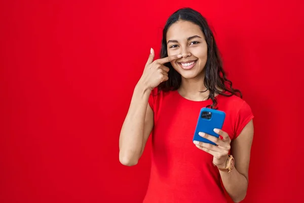 Ung Brasiliansk Kvinna Med Smartphone Över Röd Bakgrund Pekar Med — Stockfoto