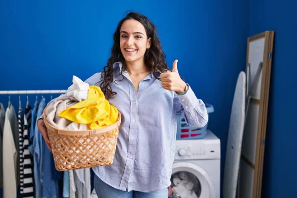 Ung Brunett Kvinna Håller Tvättkorg Ler Glad Och Positiv Tummen — Stockfoto