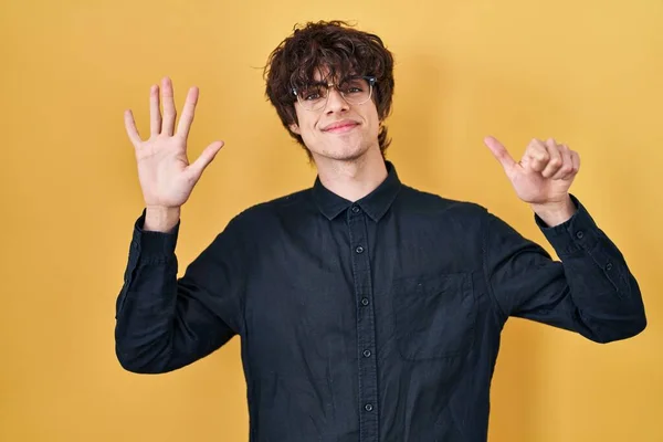 Młody Człowiek Okularach Żółtym Tle Pokazuje Wskazuje Palcami Numer Sześć — Zdjęcie stockowe