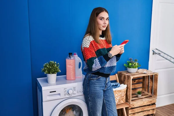 Young Woman Using Smartphone Waiting Washing Machine Laundry Room — Stock Photo, Image