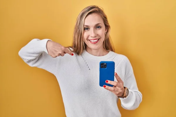 スマートフォンの入力メッセージを使用して若いブロンドの女性は 顔に笑顔で自信を持って見て 誇りに思って幸せな指で自分自身を指して — ストック写真
