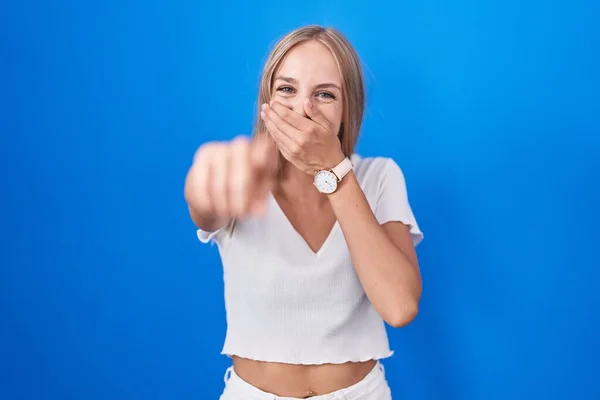 Mladá Běloška Stojí Nad Modrým Pozadím Směje Ukazuje Prstem Kameru — Stock fotografie