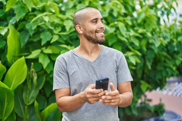 年轻的拉丁男人在公园用智能手机充满自信地微笑 — 图库照片