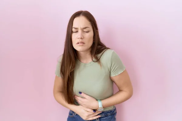 美丽的黑发女人站在粉红的背景上 双手放在肚子上 因为消化不良 痛苦不堪 疼痛的概念 — 图库照片