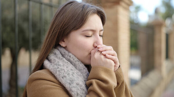 Young blonde woman blowing on hands for cold at street
