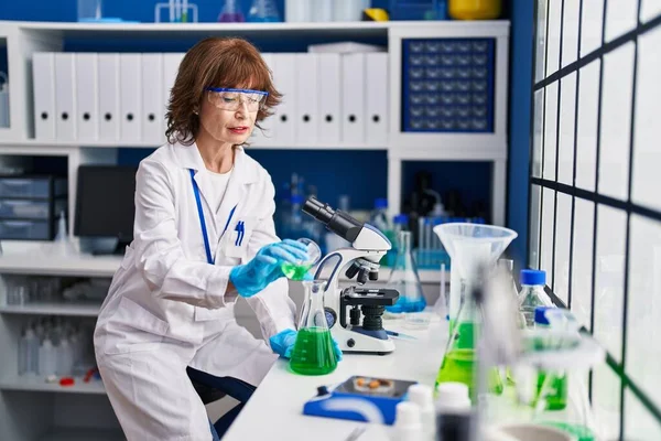 研究室で試験管に液体を注ぐ中年女性科学者 — ストック写真