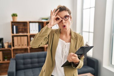 Muayenehanede çalışan genç bir kadın şaşırmış bir yüz ve parmaklarından bakan bir bakışla şok olmuş bir jest yapıyor. İnançsız ifade. 