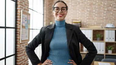 Genç, güzel, İspanyol bir iş kadını ofiste kendinden emin gülümsüyor.