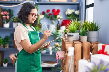 Young woman florist smiling confident writing on clipboard at florist