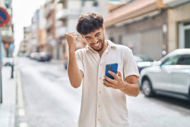 Young arab man using smartphone with winner expression at street